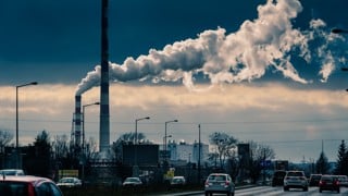 Bilar och rök från skorstenar i industriområde.