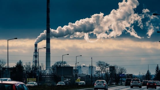 Bilar och rök från skorstenar i industriområde.