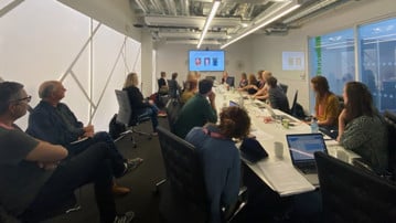A meeting table with people listening to presenter Mikaela Wikström