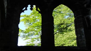 Bild innifrån kyrka på två kyrkfönster som vetter ut över en grönskande bakgrund