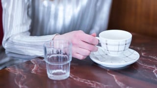 Detalj på person med kaffekopp på ett café.