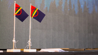 Två bordsflaggor med bild av norrsken projicerad på skärm i bakgrunden under firandet av den samiska nationaldagen på Umeå universitet 2018.