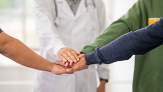 Samarbete, grupp med händer på varandra varav en läkares hand.
