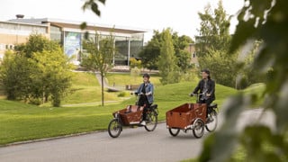 Två personer med eldriva lådcyklar som hyrs ut av Umeå kommun på campus.