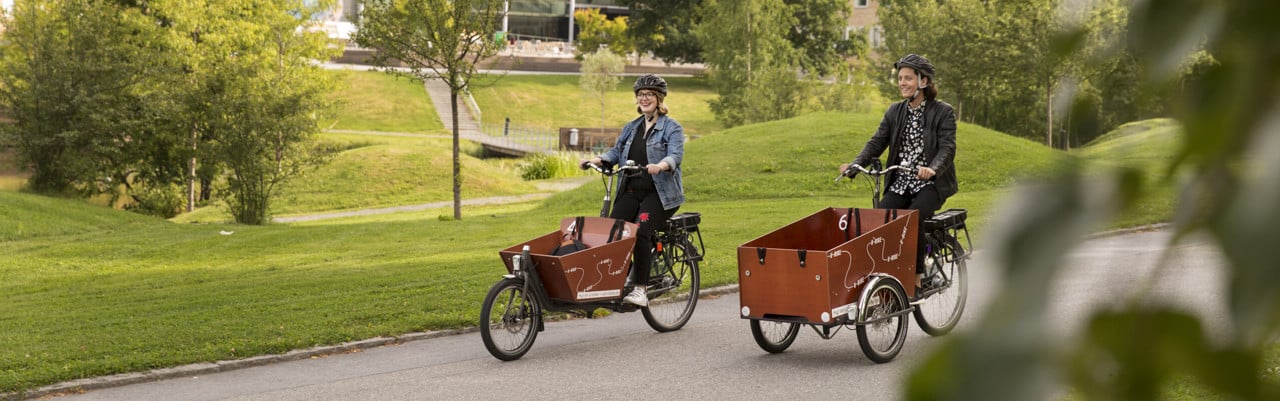 Två personer med eldriva lådcyklar som hyrs ut av Umeå kommun på campus.