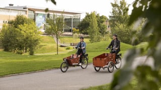 Två personer med eldriva lådcyklar som hyrs ut av Umeå kommun på campus.