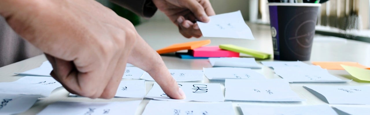 Person pekar på Post-it-lappar på ett bord.