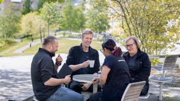 Fyra personer sitter utomhus och dricker kaffe i vårsolen.