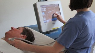 Sköterska för ultraljudsapparat över patients hals och studerar skärmen. En annan sköterska tittar på