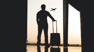 Silhuett av en person som står på en flygplats med bagage i handen.