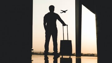 Silhuett av en person som står på en flygplats med bagage i handen.