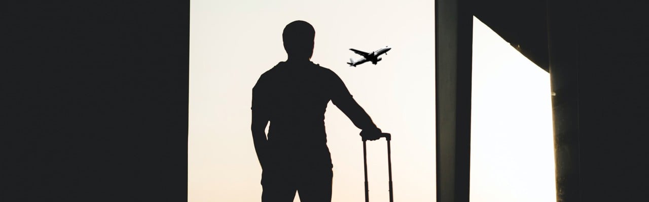 Silhuett av en person som står på en flygplats med bagage i handen.