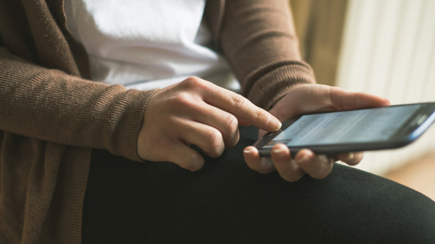 Detalj p&aring; person vars h&auml;nder h&aring;ller i en mobiltelefon som hen surfar p&aring;.